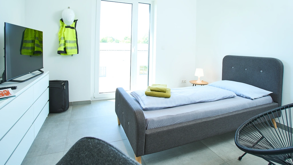 Helles Schlafzimmer mit Einzelbett, Fernseher und Warnweste