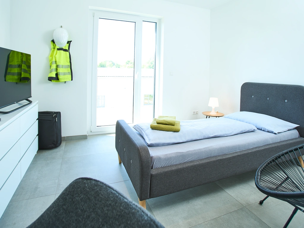 Helles Schlafzimmer mit Einzelbett, Fernseher und Warnweste