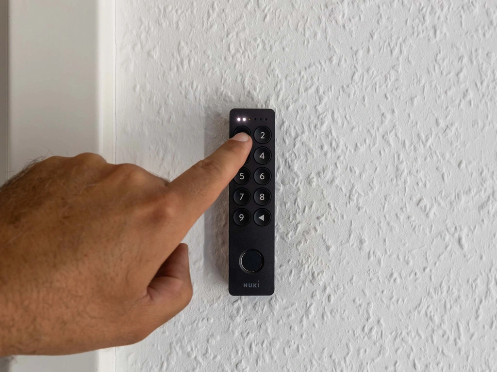 Hand drückt Knopf 2 auf schwarzer Nuki Fernbedienung an weißer Wand
