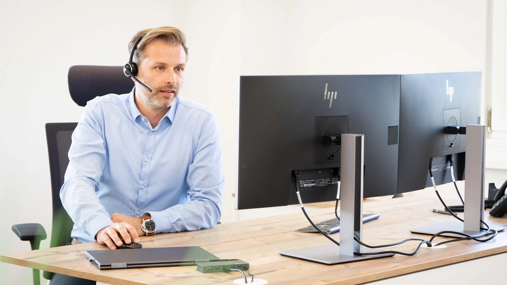 Mann mit Headset arbeitet an zwei Monitoren im Büro