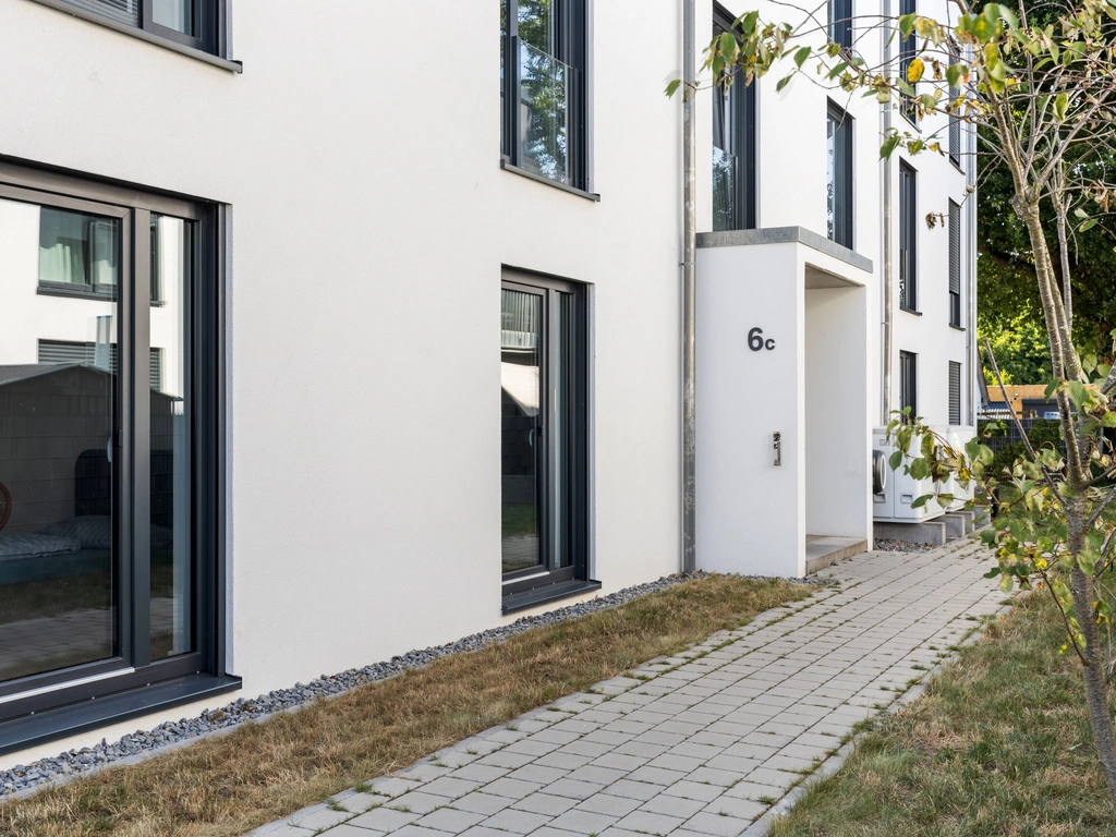 Moderner weißer Hauseingang mit der Hausnummer 6c und gepflastertem Weg