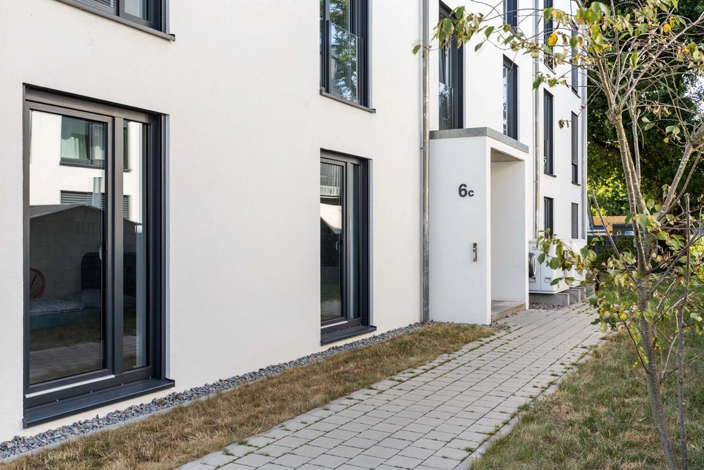 Eingang eines modernen Wohngebäudes mit weißen Wänden und schwarzem Fensterrahmen