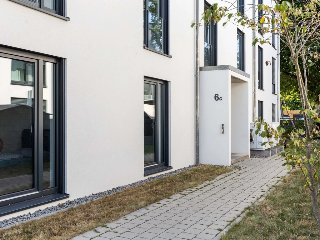Eingang eines modernen Wohngebäudes mit weißen Wänden und schwarzem Fensterrahmen