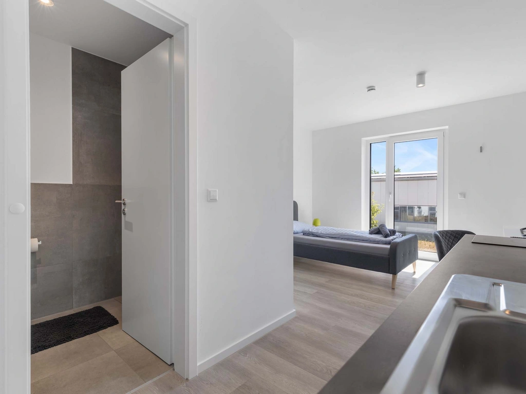 Moderner weißer Wohnraum mit offener Tür zum Badezimmer und Sofa am Fenster