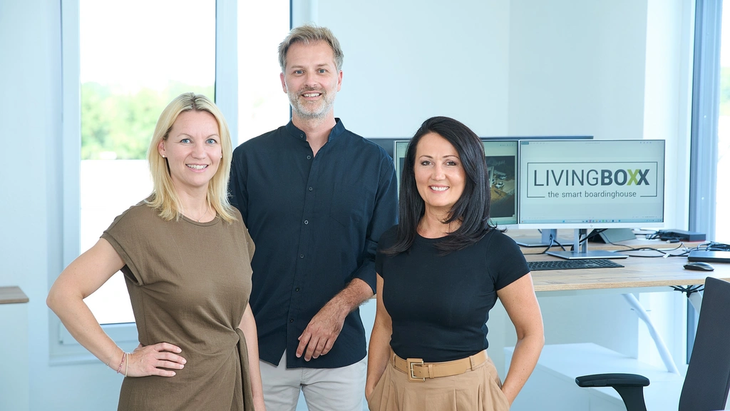 Drei Personen in einem Büro neben einem Bildschirm mit LIVINGBOXX-Logo