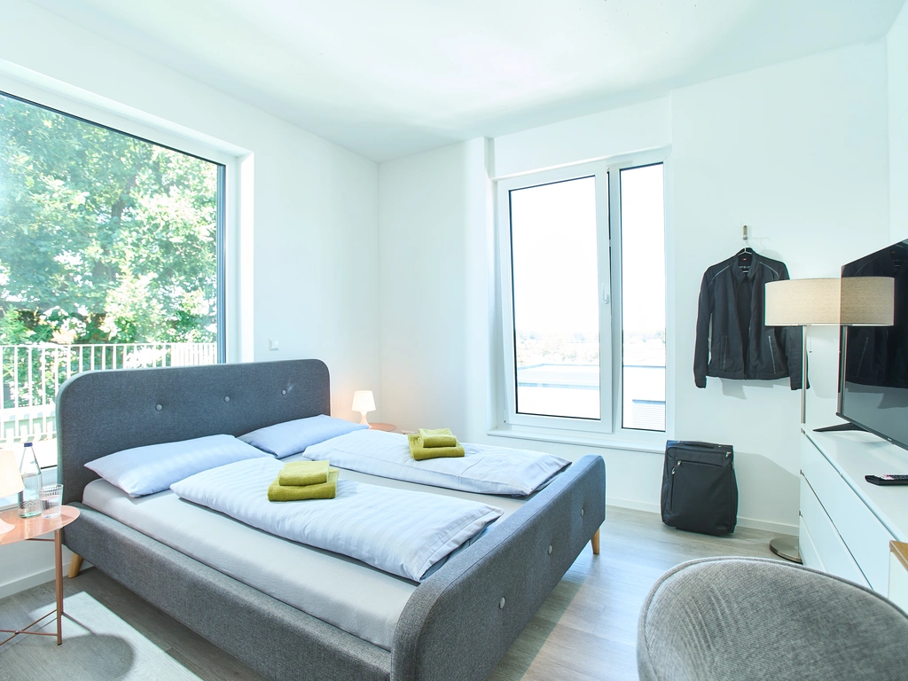 Helles Schlafzimmer mit Doppelbett, Sesseln, Koffern und großen Fenstern