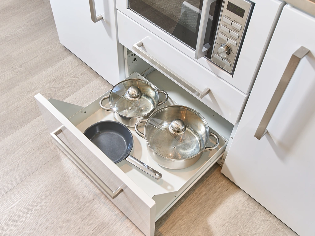 Geöffnete Küchenschublade mit zwei Töpfen und einer Pfanne unter einer Mikrowelle