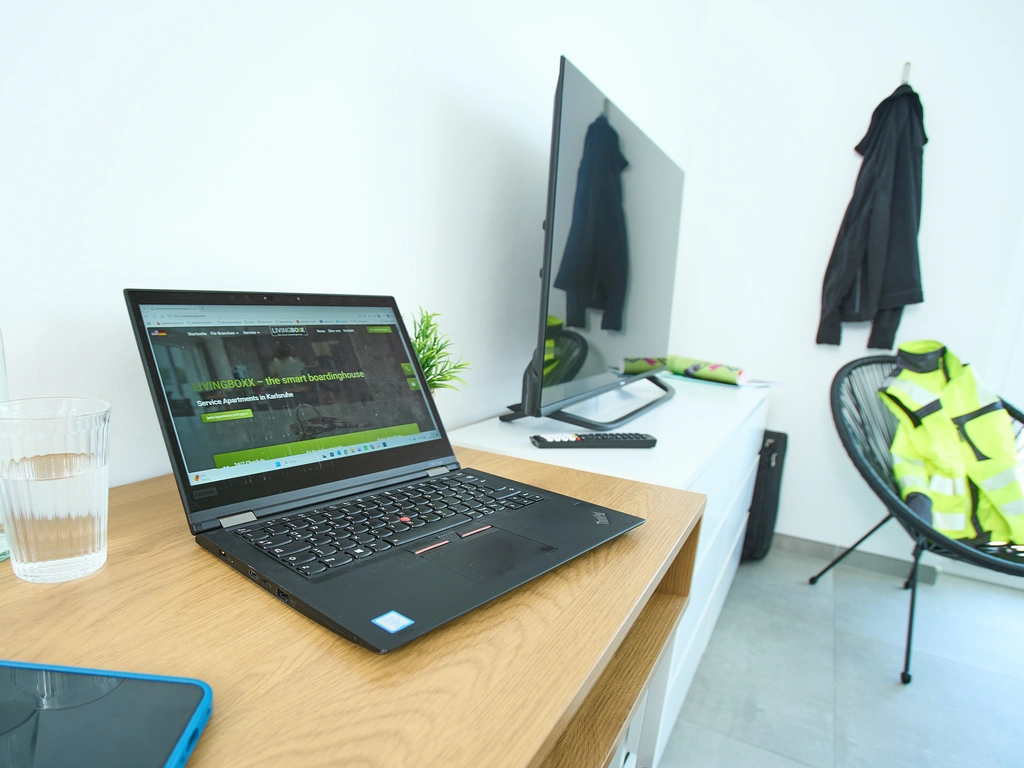 Arbeitsplatz mit Laptop, Monitor, Wasserglas und Kleidung auf einem Stuhl