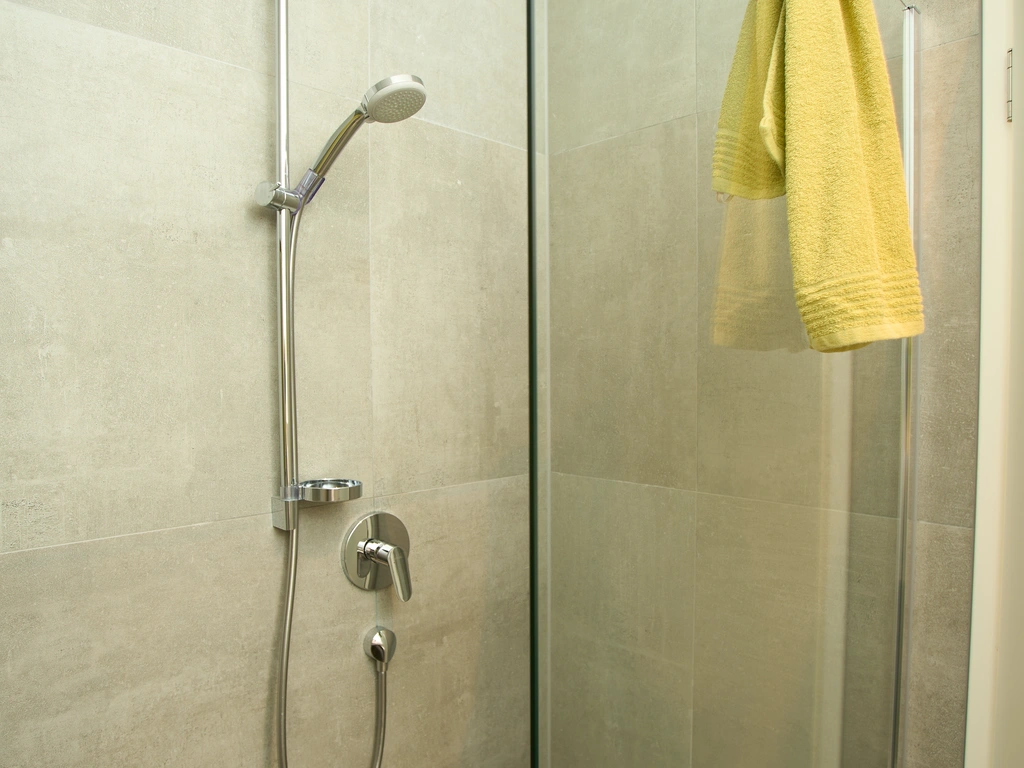 Gläserne Dusche mit Handbrause und gelbem Handtuch