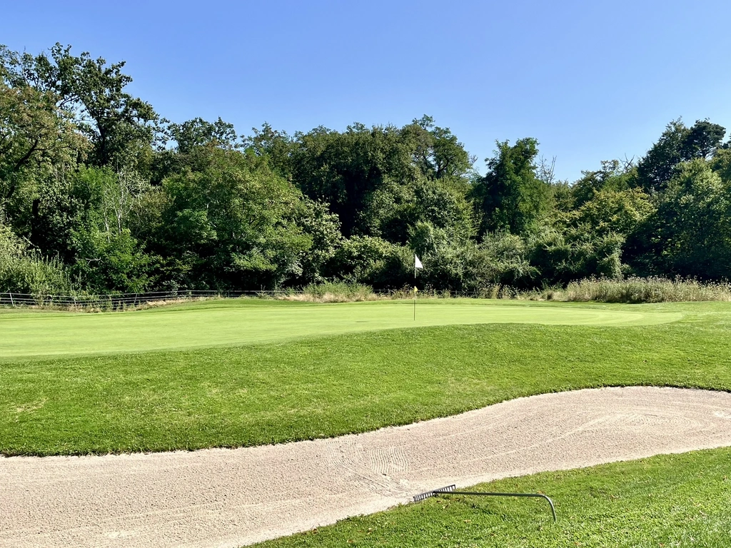 Golfplatz mit grünem Gras, Sandbunker und Bäumen im Hintergrund