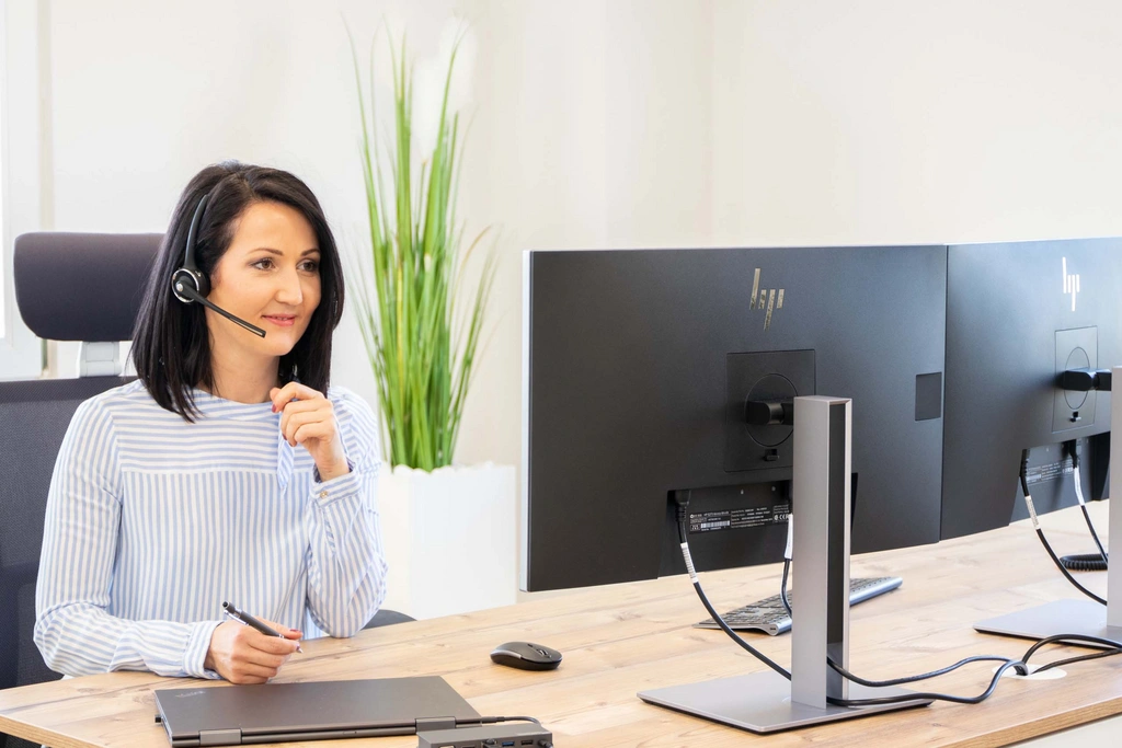 Frau mit Headset arbeitet an zwei Computern im Büro