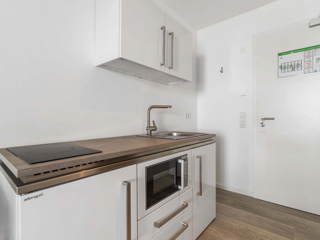 Kleine moderne Küche mit Kochfeld, Spüle und Hochschrank in weißem Raum
