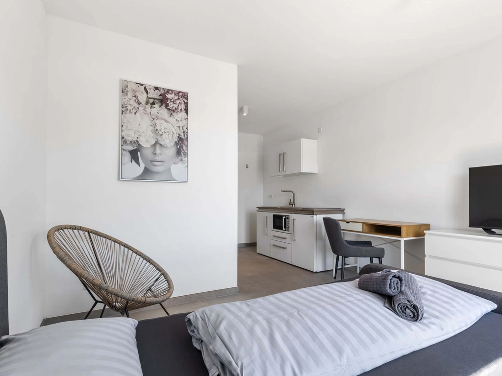 Moderner, minimalistisch eingerichteter Raum mit Bett, Küche und Schreibtisch