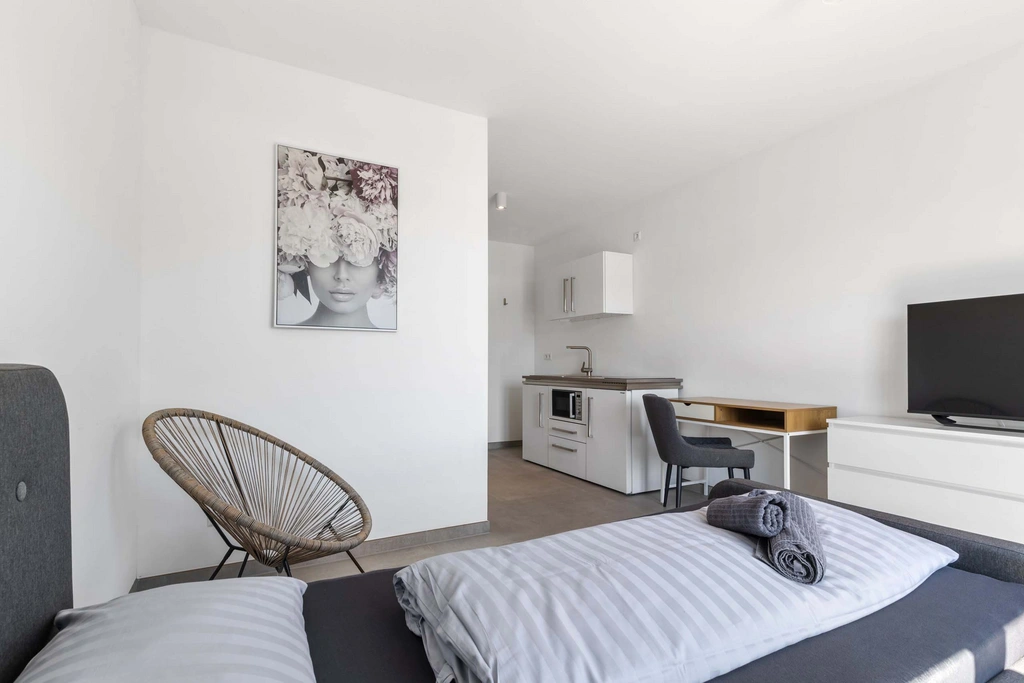 Moderner, minimalistisch eingerichteter Raum mit Bett, Küche und Schreibtisch