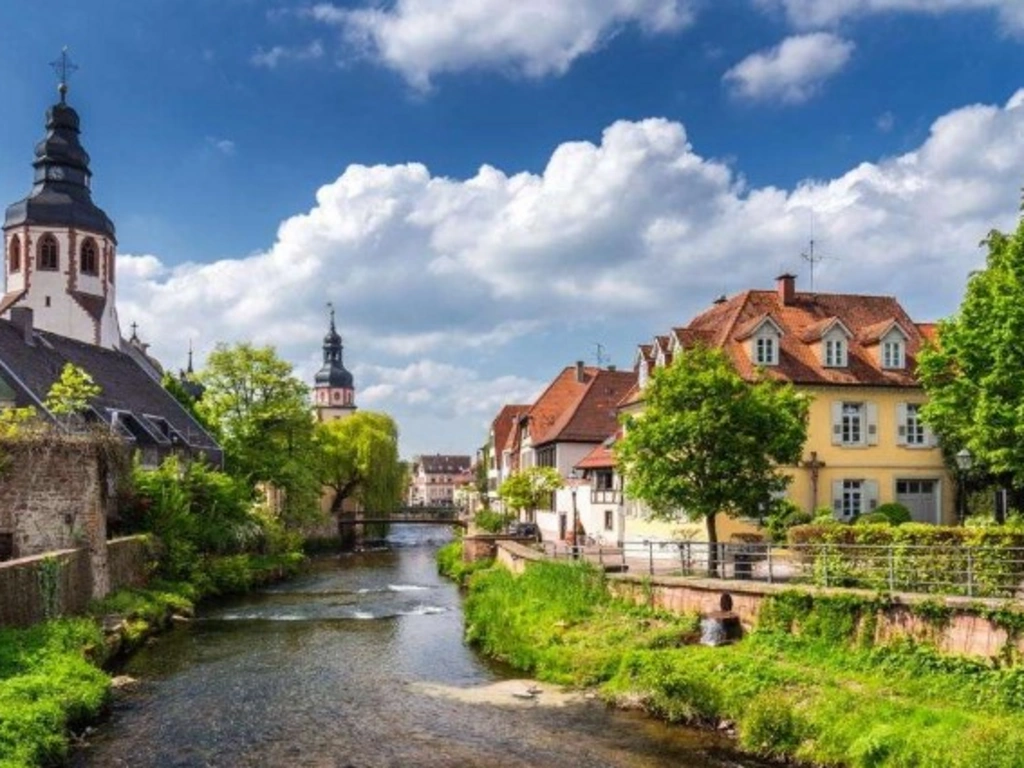 Fluss mit Häusern und Kirchtürmen unter blauem Himmel mit Wolken