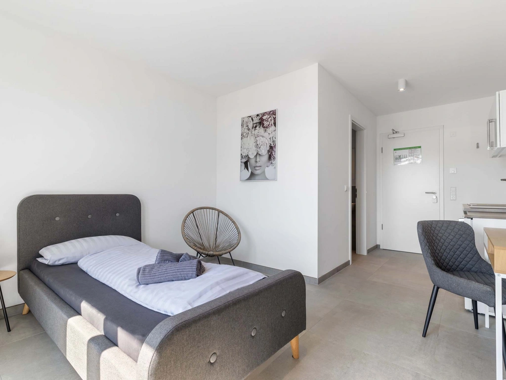Modernes Einzelzimmer mit grauem Bett und Küchenzeile