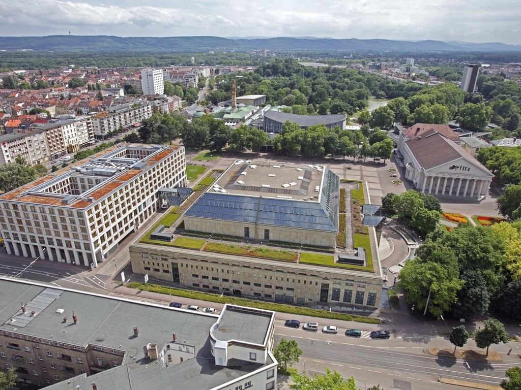 Luftaufnahme einer Stadt mit Park, markanten Gebäuden und bewaldeten Hügeln im Hintergrund