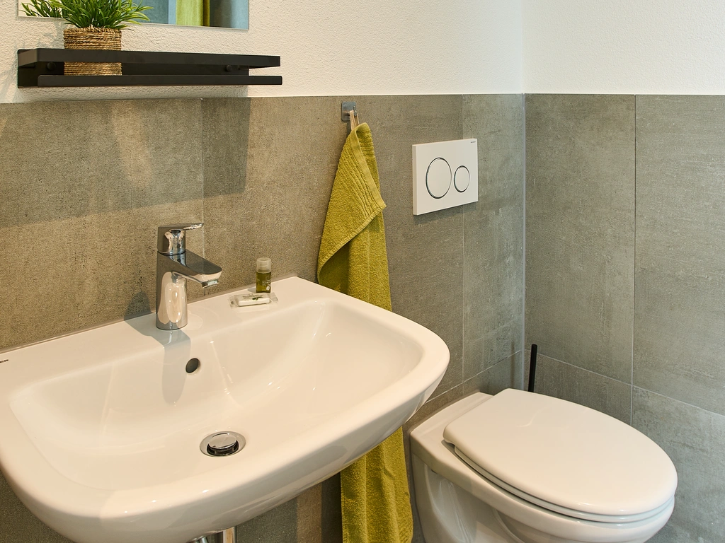 Modernes Badezimmer mit Waschbecken, WC, Spiegel und grünem Handtuch