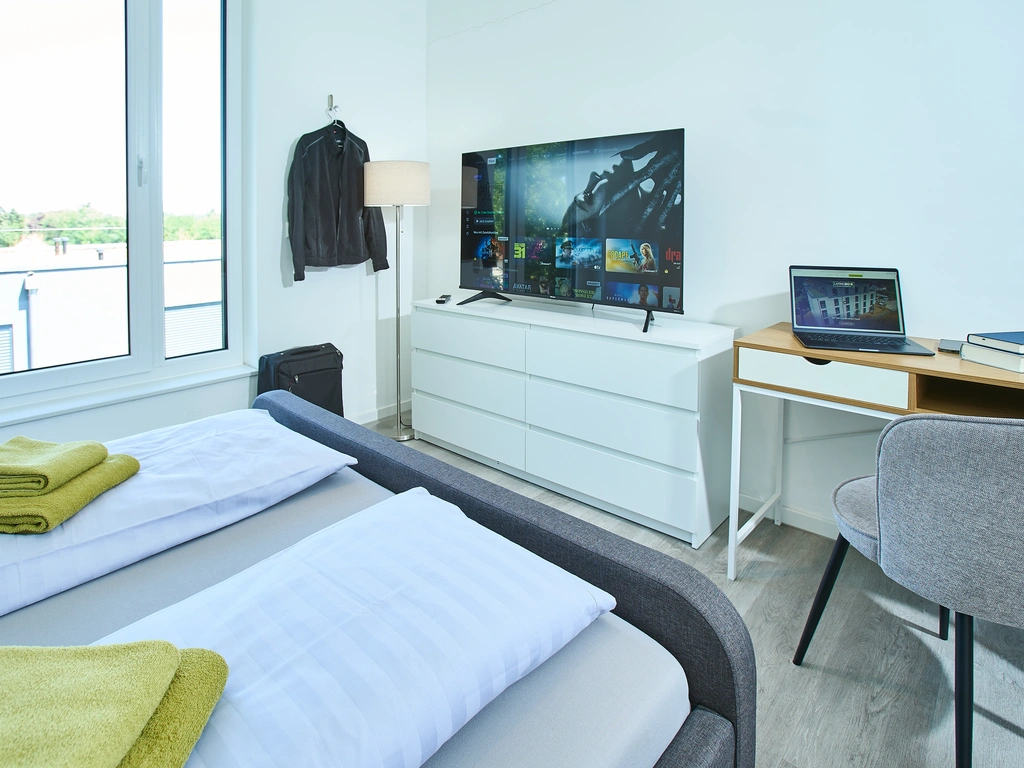 Helles Zimmer mit Bett, Fernseher, Schreibtisch und Laptop